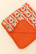 Close up of a bamboo reversible blanket orange and white stripe, with white daisy's on top  and the reverse side a bright orange against a beige background