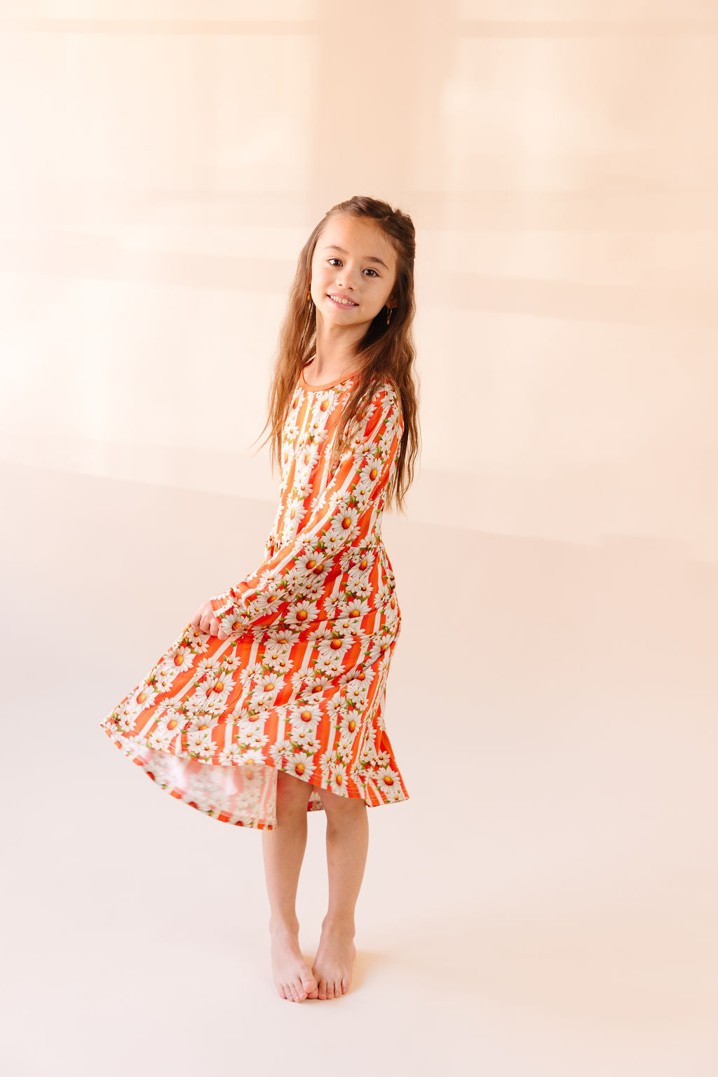 Young girl twirling wearing a orange and white stripe floral dress against a plain background