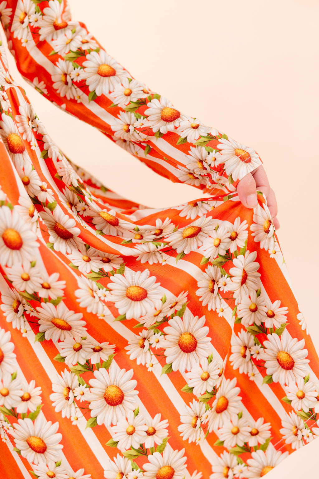 Close up of Young girl in bamboo twirl dress wearing a bamboo Twirl dress with orange and white stripe, with white daisy's on top  and the reverse side a bright orange against a beige background