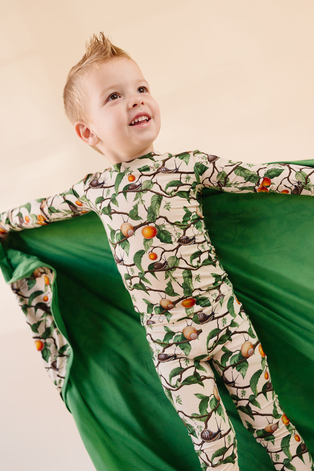 Boy wearing snail and apricot pattern bamboo pajamas holding matching bamboo blanket, showing the green backing