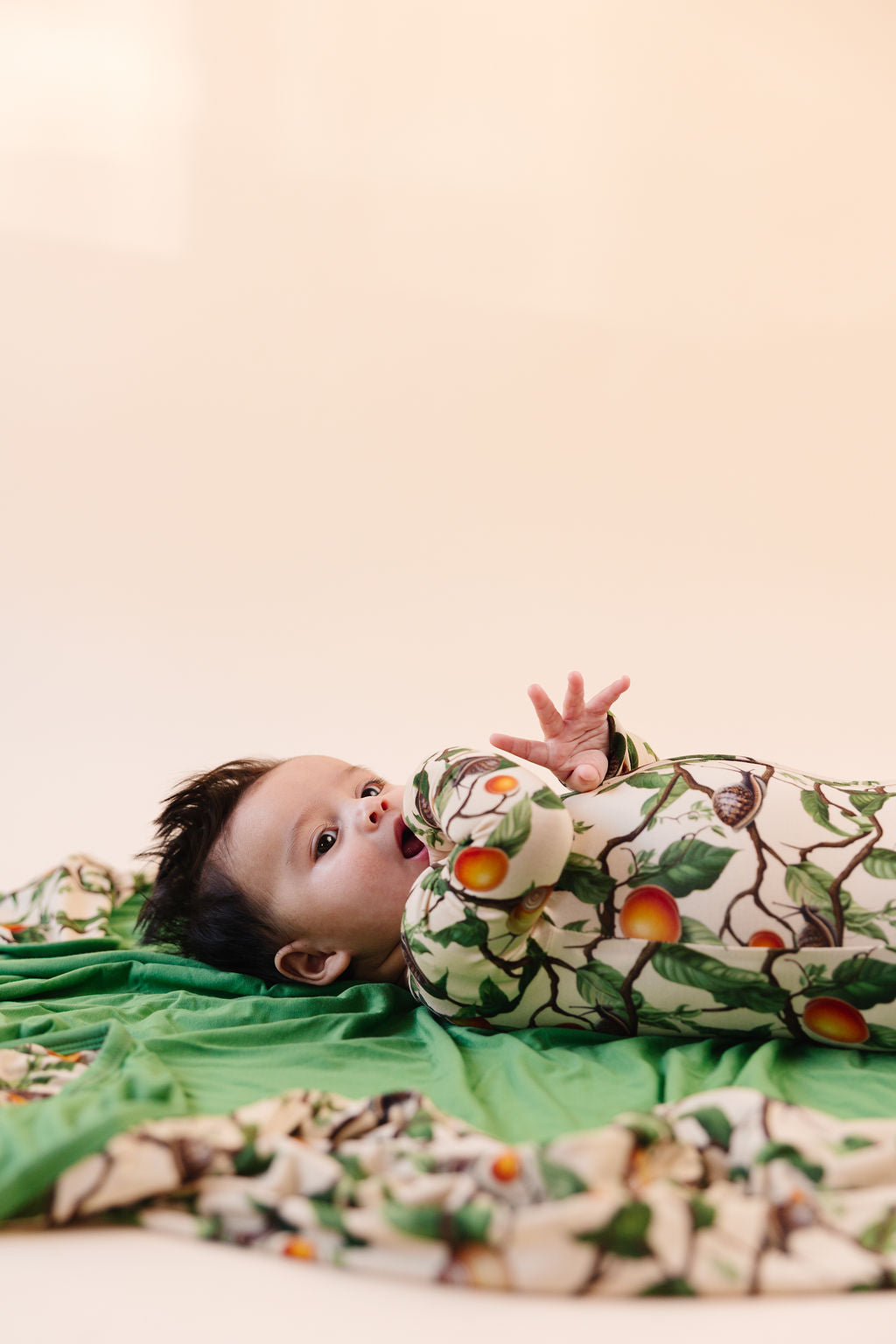 Baby in snail pattern bamboo romper lying on a green blanket with the revered side the same snail pattern against a beige background