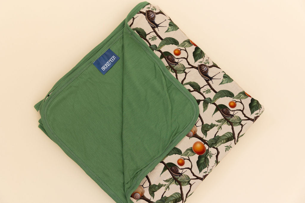 Boy wearing snail and apricot pattern bamboo pajamas holding matching bamboo blanket, showing the green backing