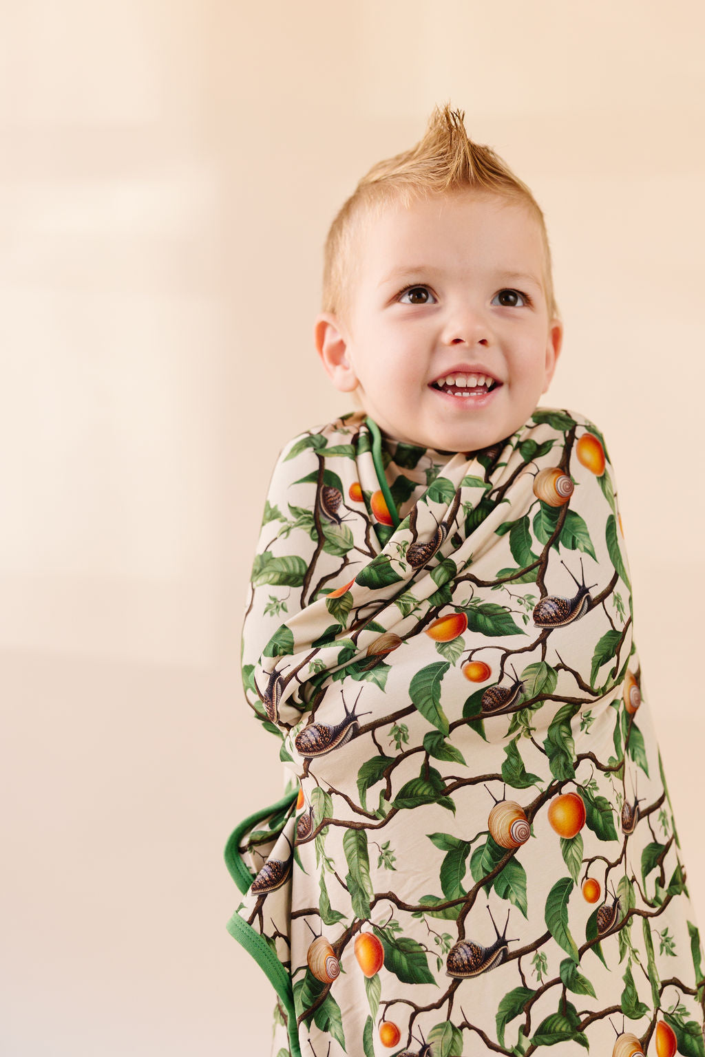 Child wrapped in a 50x50" bamboo blanket with a snail and apricot pattern on a beige background