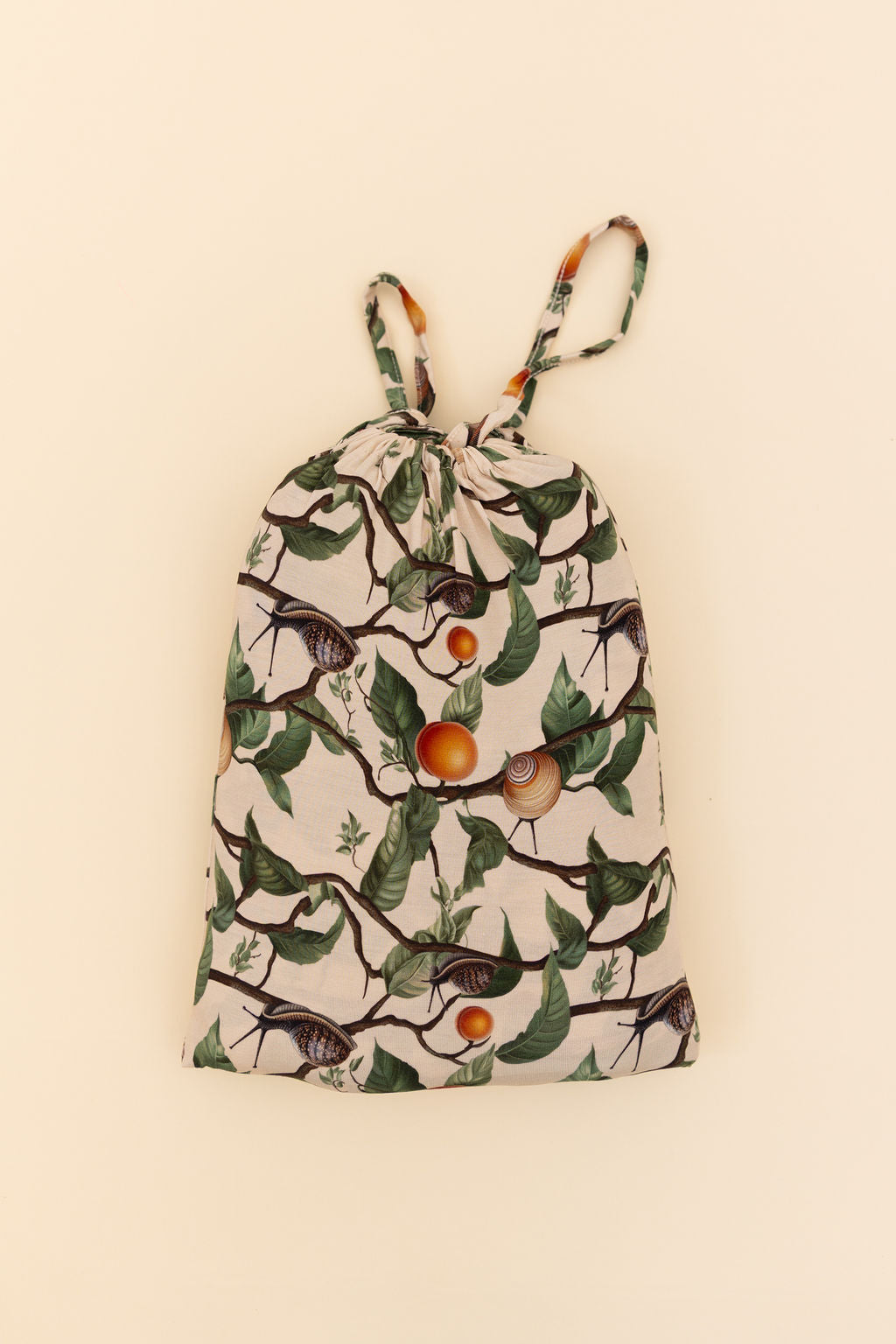 The drawstring bag that holds the 50x50 bamboo blanket. Nature-themed snail, apricot, leaves and branches print on a beige background