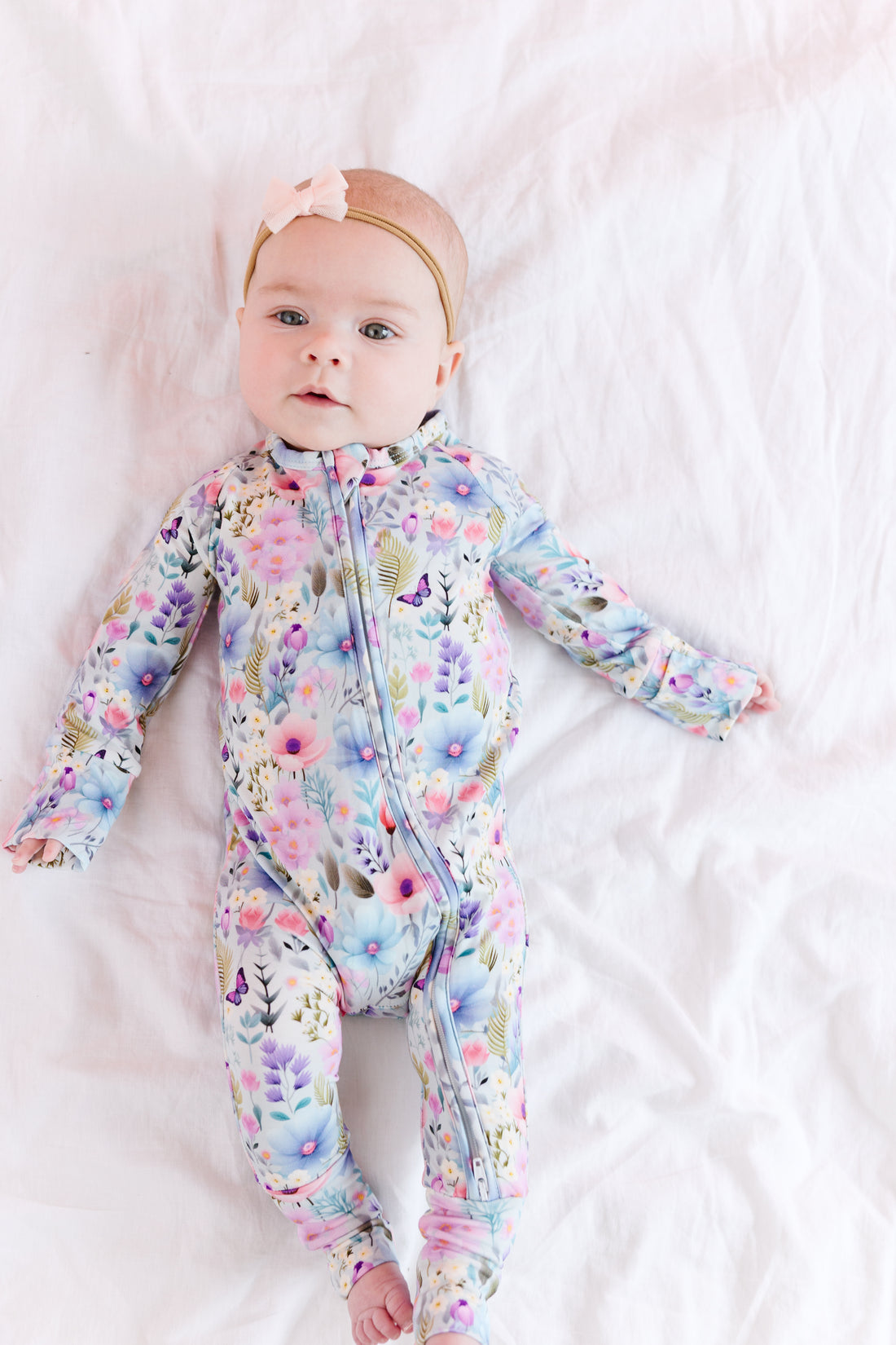 A baby lying on a white surface wearing a springtime floral convertible romper with a double zipper.