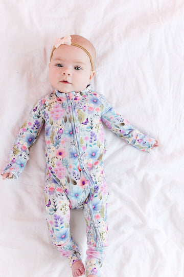A baby lying on a white surface wearing a springtime floral convertible romper with a double zipper.