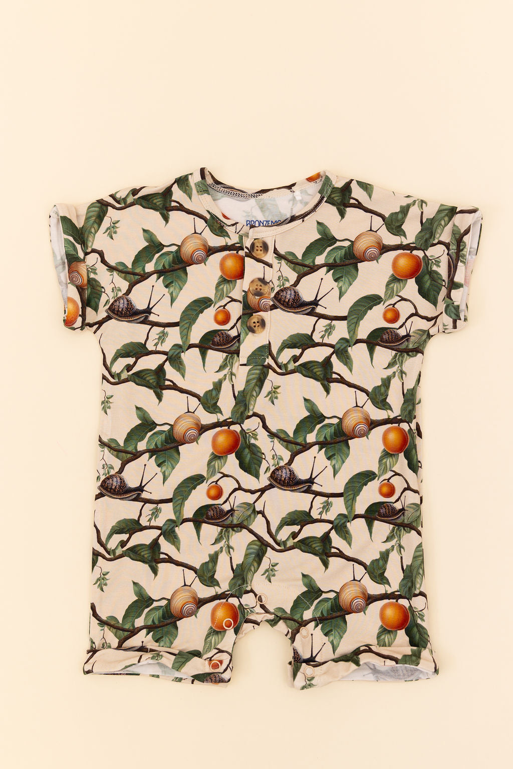 Flat lay image of Snails and apricots on branches on a short sleeve, short, henley top baby romper