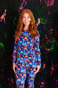 Person wearing a colorful mushroom-patterned outfit against a black background with paint splashes.