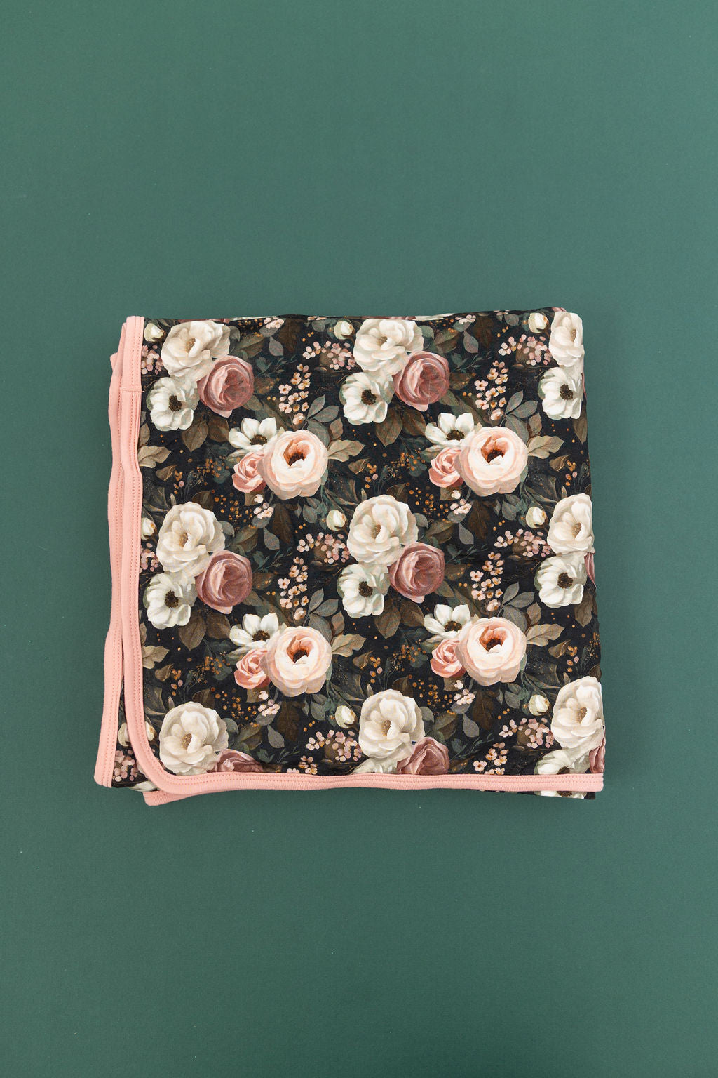 Reverie floral bamboo blanket with cream, blush, and dusty rose flowers on a dark green background