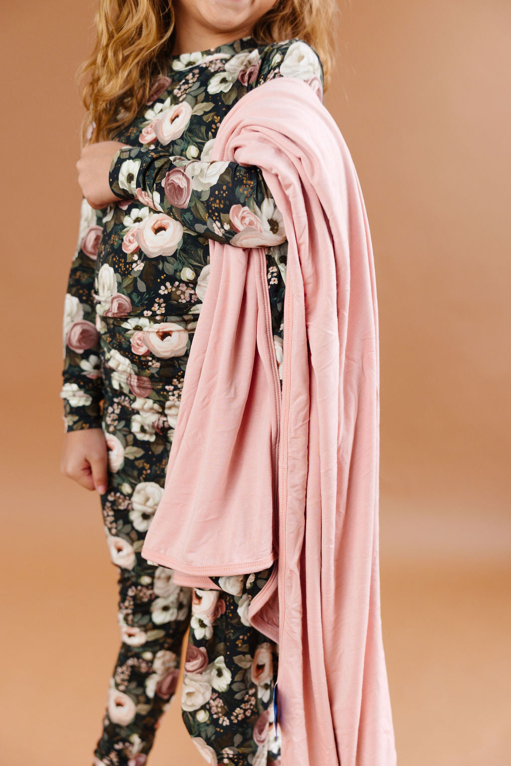 Reverie floral bamboo blanket with cream, blush, and dusty rose flowers on a dark green background